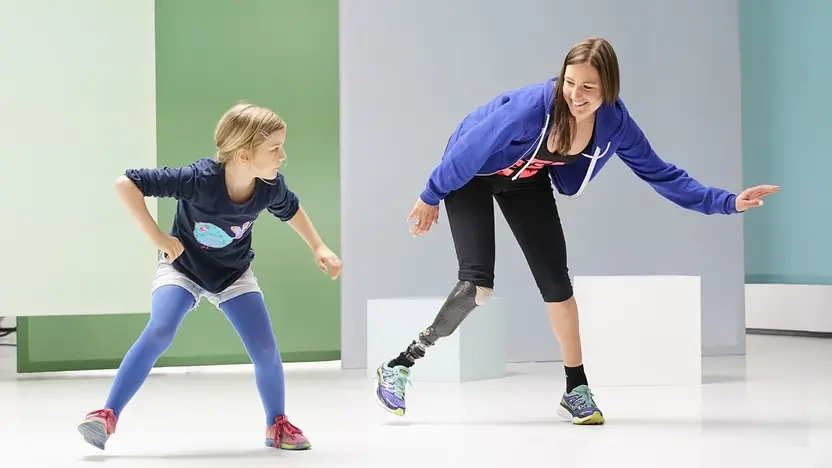 Eine junge Frau mit Beinprothese und ein Mädchen tanzen nebeneinander.