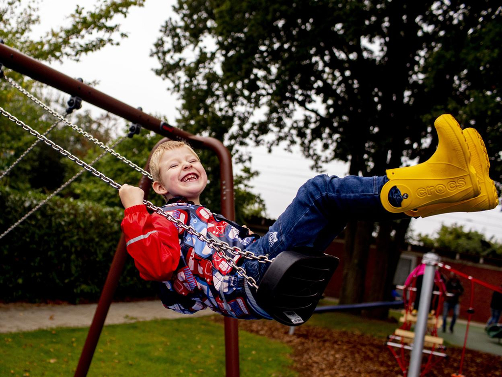 Ein Junge in gelben Gummistiefeln sitzt lachend auf einer Schaukel.