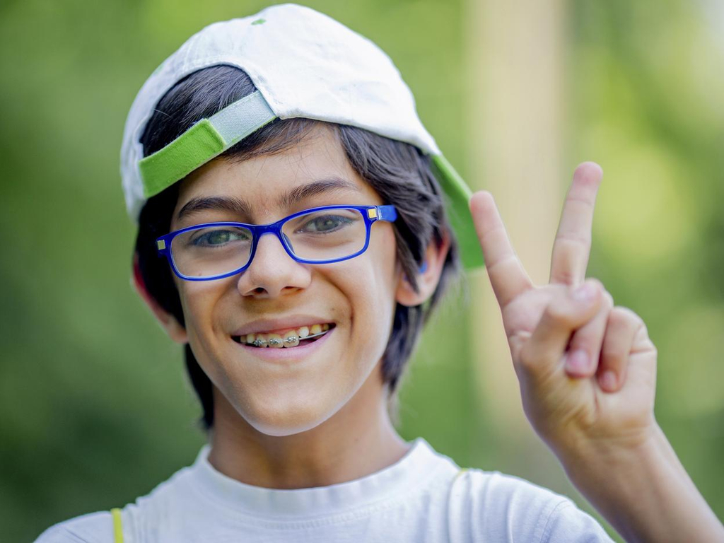 Ein Junge mit Brille und Zahnspange lacht in die Kamera. Er zeigt das Siegeszeichen.