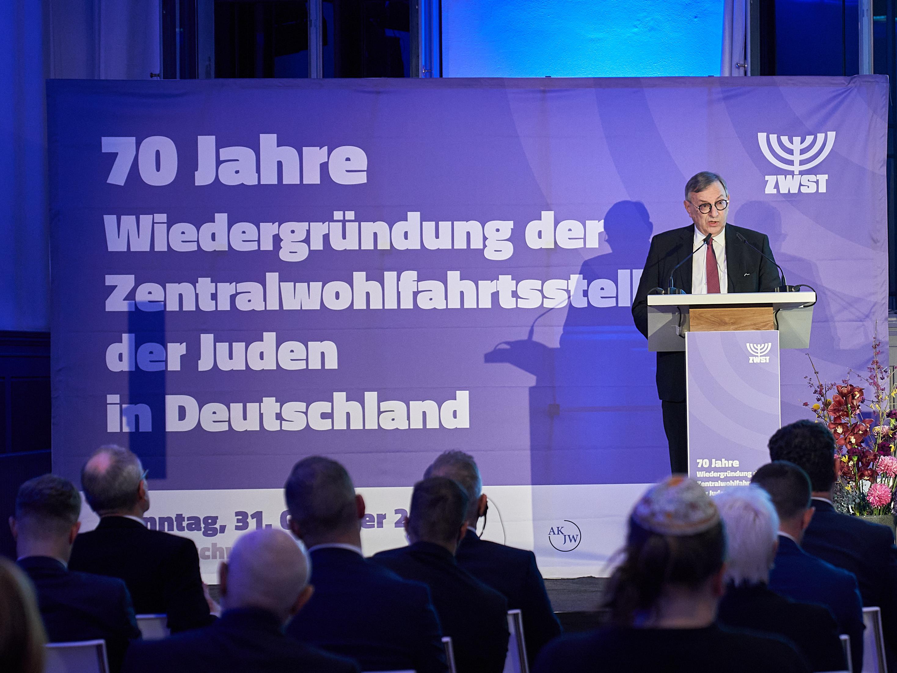 Auf einer Bühne hält Abraham Lehrer eine Rede. Hinter ihm steht ein Banner mit der Aufschrift: 70 Jahre Wiedergründung der Zentralwohlfahrtsstelle der Juden in Deutschland.