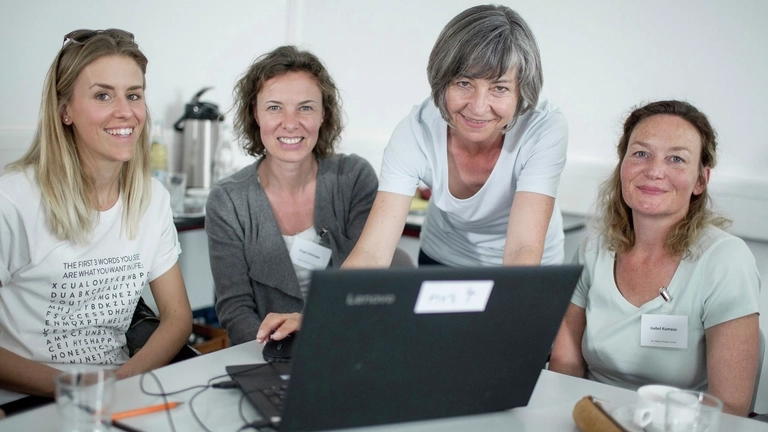 Frauen, die gemeinsam an einem Computer arbeiten, lachen in die Kamera.