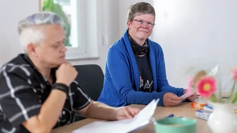 Zwei Personen sitzen an einem Tisch und arbeiten an einer Vorlage.