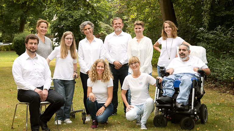 Gruppenfoto mit zehn Frauen und Männer in weißen Oberteilen im Garten