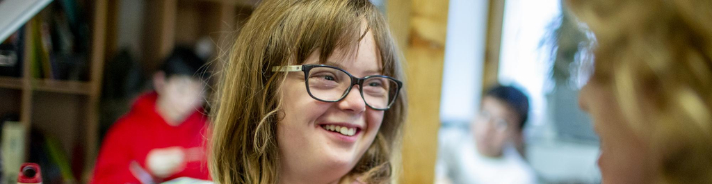 Ein Mädchen mit einem Block in der Hand schaut lächelnd zur Seite.