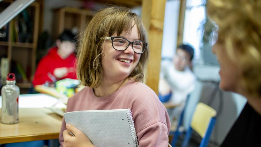 Ein Mädchen mit einem Block in der Hand schaut lächelnd zur Seite.