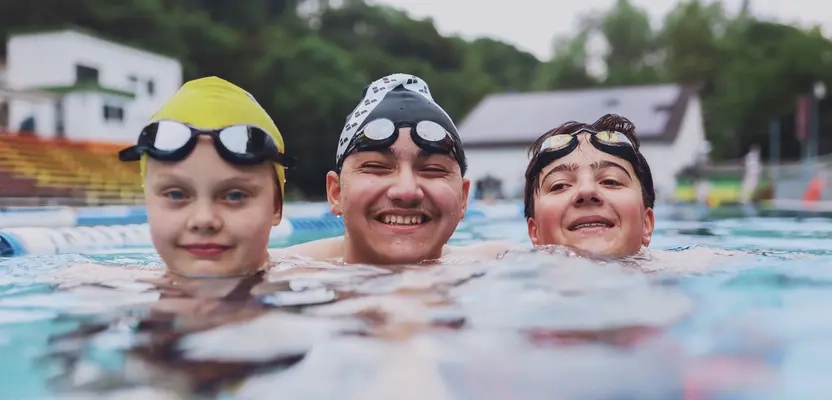Zwei Jungen und ein Mädchen schwimmen im Schwimmbecken.