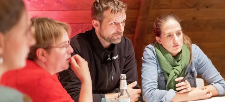 Vier Personen sitzen an einem Tisch und schauen konzentriert