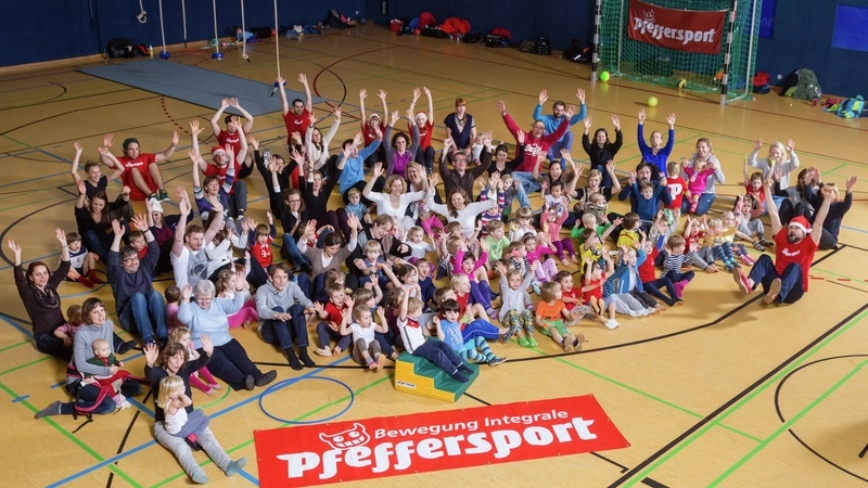 Eine große Gruppe Menschen in der Mitte einer Sporthallte. Vor ihnen liegt ein Plakat mit der Aufschrift "Bewegung Integrale Pfeffersport"