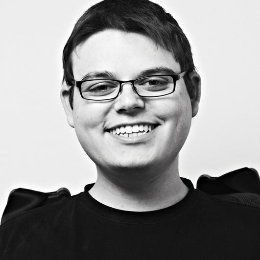 Ein junger Mann mit dunklen kurzen Haaren und Brille lächelt in die Kamera.