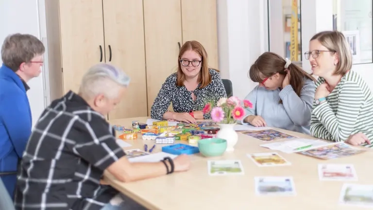 Fünf Personen sitzen an einem Tisch, sie basteln, schreiben und reden