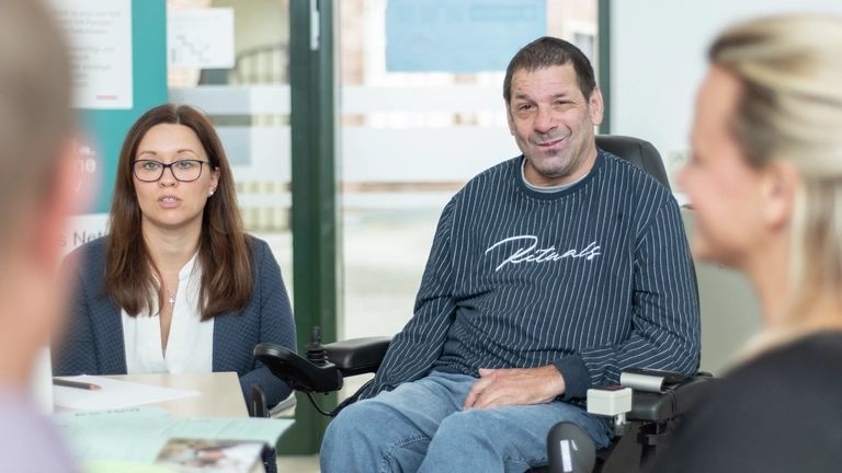 Ein Mann im Rollstuhl sitzt in einer Runde von Menschen, die diskutieren.