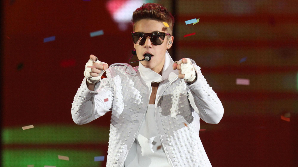 Justin Bieber in weißen Klamotten und Sonnenbrille singend auf der Bühne