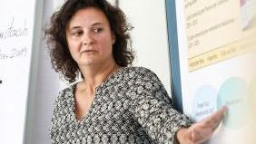 Eine Frau hält einen Vortrag. Sie zeigt auf eine Info-Tafel mit Text und Grafiken.