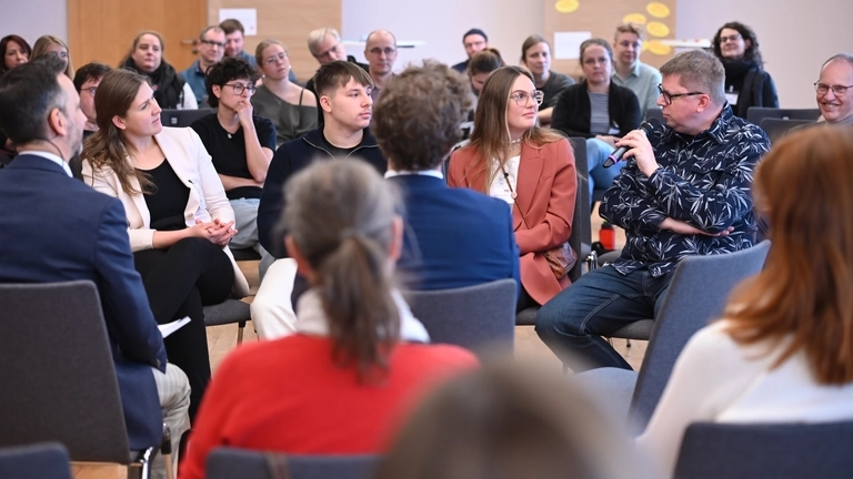 Viele Menschen sitzen auf Stühlen und hören einer Diskussion zu