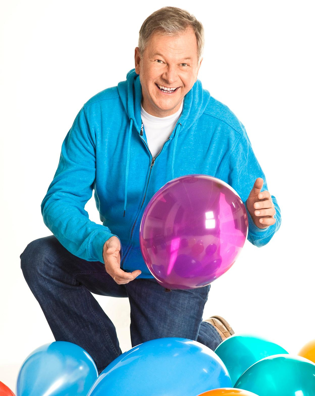 Ein Porträtfoto von dem Kinderliedermacher Reinhard Horn, der einen violetten Luftballon in den Händen hält.