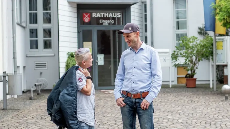 Zwei Personen stehen vor dem Rathaus in Nieder-Olm und unterhalten sich.