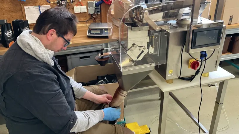 Dunkelhaariger Mann mit Brille füllt an einer Maschine Kaffee in Tüten