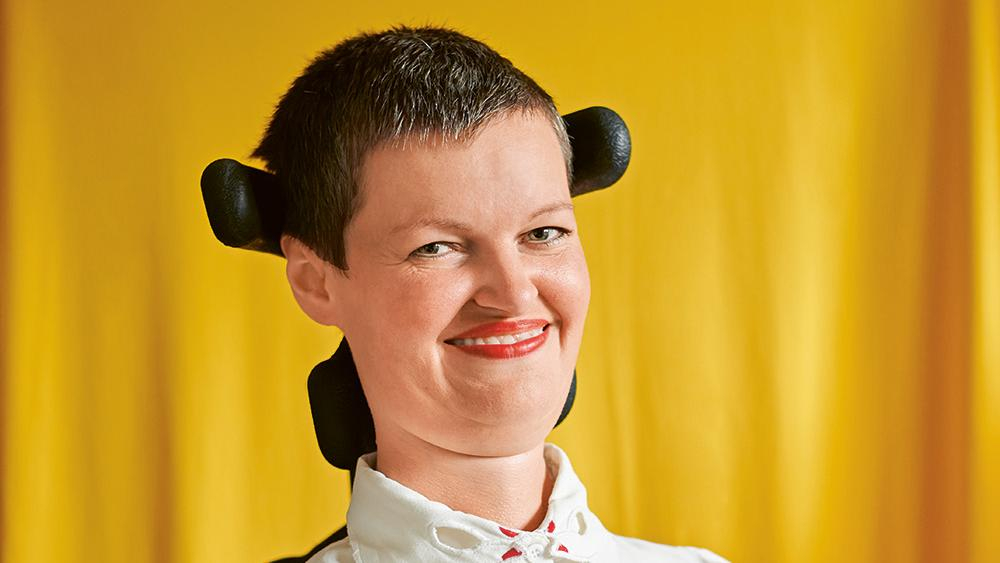 Eine Frau mit kurzen Haaren im Rollstuhl lächelt