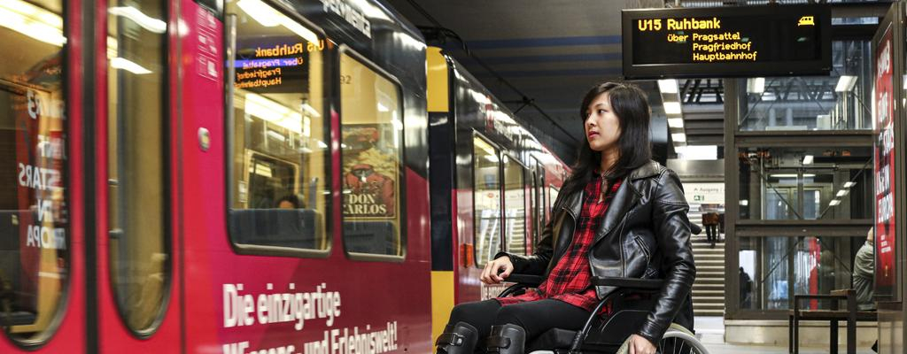 Simone mit ihrem Rollstuhl an einer U-Bahn-Haltestelle. Die Bahn ist gerade eingefahren.