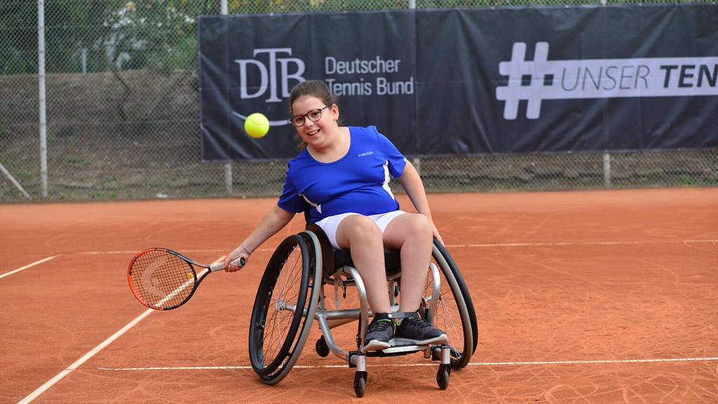 Mädchen beim Tennistraining mit Rollstuhl auf dem Sandplatz