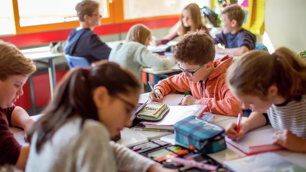 Schüler*innen sitzen in Vierergruppen in einem Klassenzimmer und bearbeiten Aufgaben in ihren Heften. 