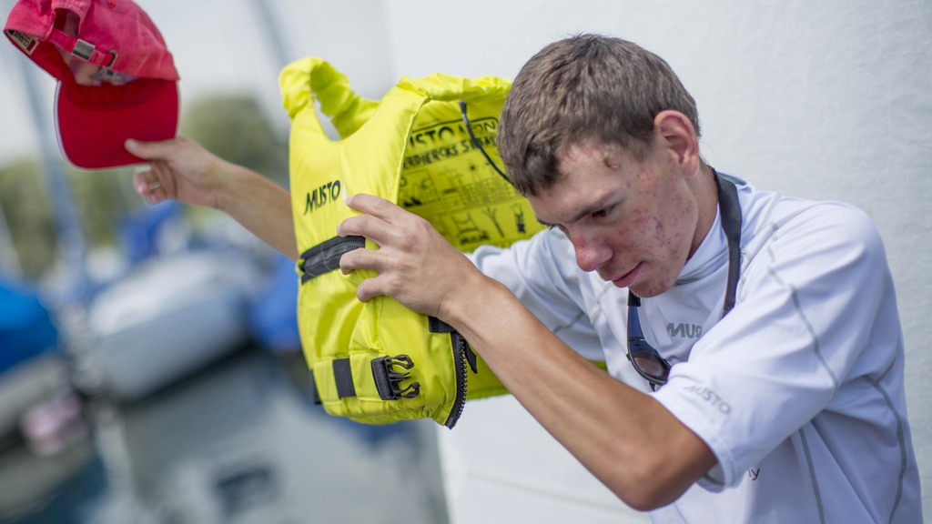 Ein junger Mann mit Behinderung zieht eine gelbe Schwimmweste an.