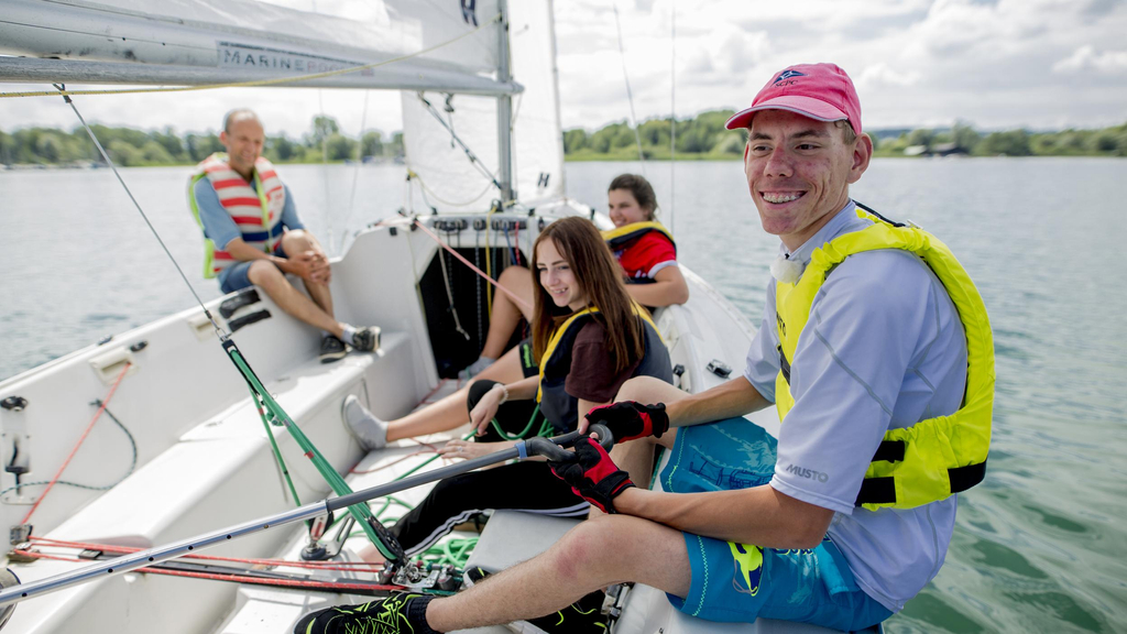 Vier Jugendliche und ein Mann sitzen auf einem Segelboot.