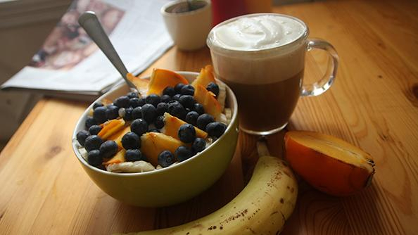 Schmackhaftes Frühstücksbild mit einer Schüssel Obstsalat, Kaffee und Banane.