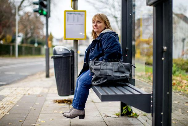 Eine Frau sitzt auf einer Bank an einer Bushaltestelle.