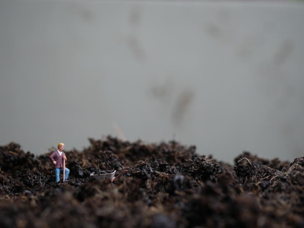 Ein kleines Männchen steht mit Spaten und Schubkarre auf matschiger Erde.