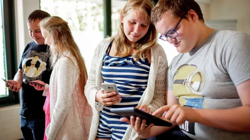 Vier Kinder stehen nebeneinander. Jedes hat ein Smartphone oder ein Tablet in der Hand auf das sie schauen.