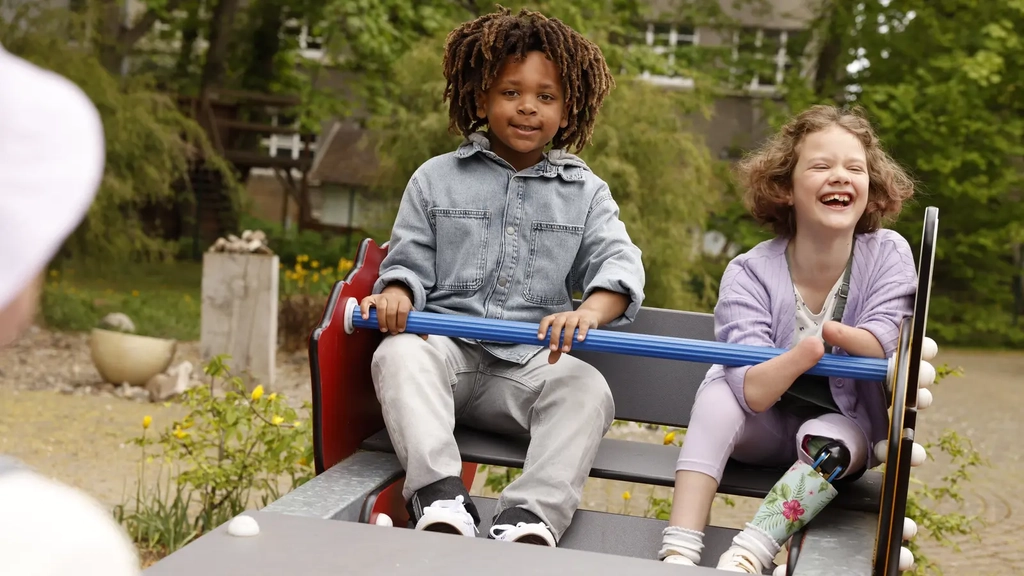 Ein Mädchen mit Beinprothese und ein schwarzer Junge sitzen auf einer Wippe