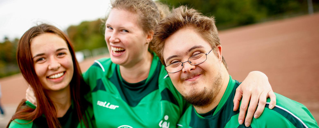 Drei junge Menschen in Sporttrikots umarmen sich