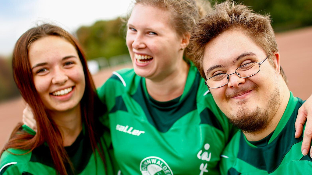 Drei Jugendliche in Sporttrikot umarmen sich.
