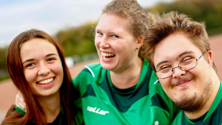 Drei Jugendliche in Sporttrikot umarmen sich.