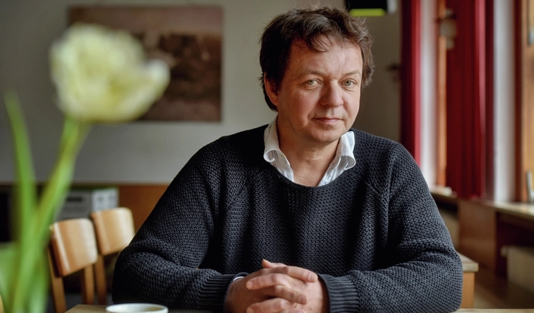 Stefan Reichmann sitzt an einem Tisch und schaut in die Kamera.