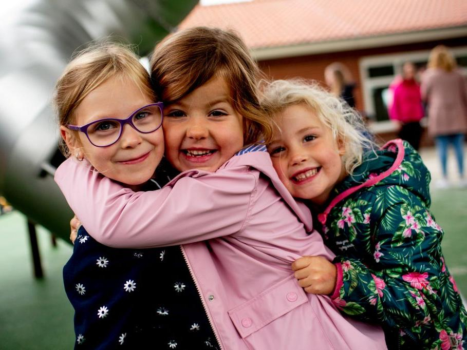 Drei Mädchen im Kindergarten umarmen sich herzlich und lachen in die Kamera.