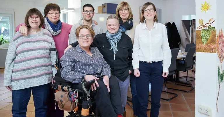 Eine Gruppe von Menschen schauen fröhlich in die Kamera.