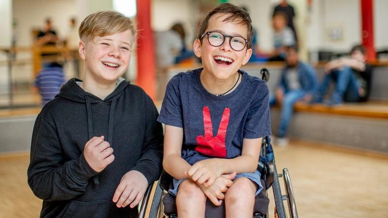 Zwei Jungen, einer davon im Rollstuhl, lachen gemeinsam.