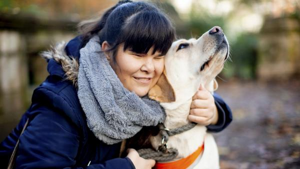 Eine junge Frau in winterlicher Kleidung hockt neben ihrem Blindenhund und krault ihn zärtlich.