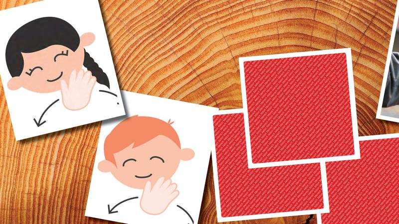 Vier Karten des InkluMemo-Spiels liegen aufgedeckt auf einem Holztisch. Drei davon liegen zugedeckt auf dem Tisch, ihre Rückseite ist rot-weiß gemustert.