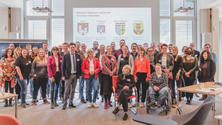 Eine Gruppe von Menschen steht vor einer Präsentationswand, auf der vier unterschiedliche Wappen zu sehen sind.