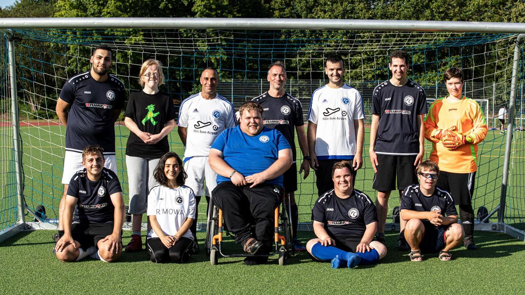 Spieler*innen des FC Germania Zündorf posieren mit dem Trainer*innenteam vor einem Fußballtor.