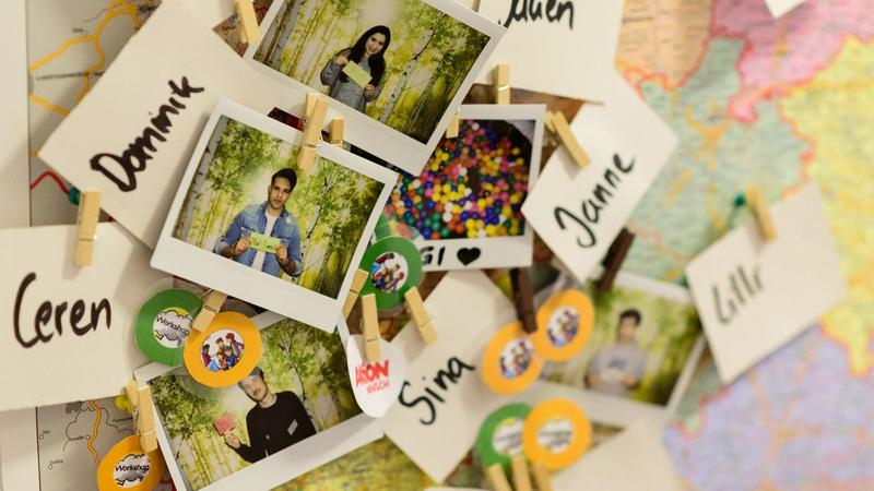 Eine Pinnwand mit Bildern junger Menschen, Namensschildern und bunten Buttons.