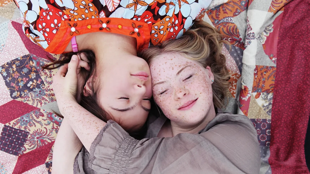 Blick von oben: zwei Mädchen liegen auf einer Decke  mit ihren Köpfen dicht beieinander. 