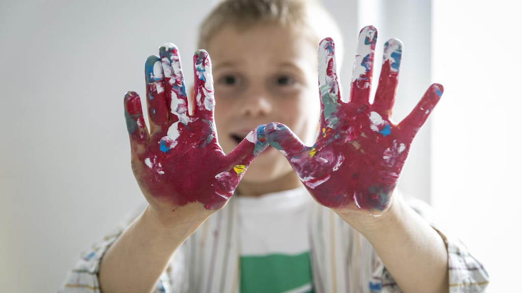 Ein Junge hält seine Hände vor sich. Sie sind mit pinker Farbe bedeckt. 