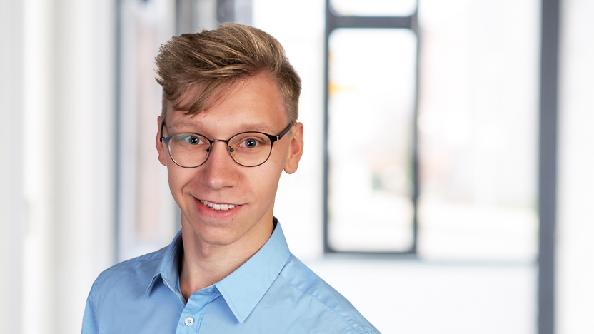 Philip Oettel, ein junger Mann mit blonden Haaren und Brille, lächelt in die Kamera.