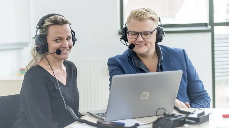 Eine Frau und ein Mann haben ein Headset auf dem Kopf und nehmen an einer Video-Konferenz am Laptop teil.