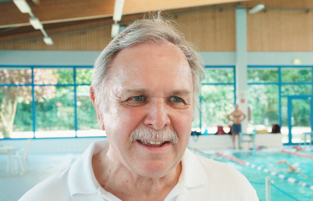 Porträt eines Mannes der vor einem Schwimmbecken steht.
