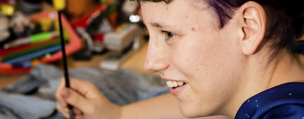 René sitzt an seinem Schreibtisch und malt mit einem Pinsel.